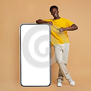 Happy Black Man Leaning And Pointing At Big Smartphone With White Screen photo