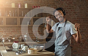 Happy black man listening to music and dancing in kitchen