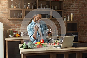 Happy black man looking at laptop and cooking dinner