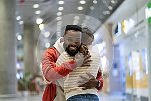 Happy black man meeting girlfriend in airport after long time, couple hugging at arrival gate