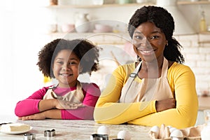 Happy Black Mom And Daughter In Aprons Sitting At Table In Kitchen