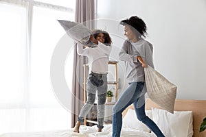 Happy black mom and daughter have pillow fight on bed