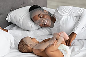 Happy black mom lying in bed with her cute infant