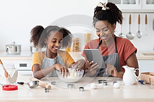 Happy black mother and daughter baking together, reading culinary blog
