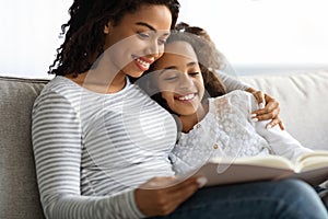 Happy black mother and daughter reading book together