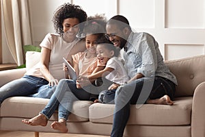 Happy black parents and children using digital tablet on sofa