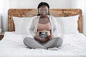 Happy black pregnant woman sitting on bed with her baby sonography photo