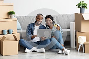 Happy black spouses purchasing furniture online after moving to new apartment