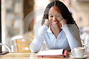 Happy black student memorizing notes in a bar terrace photo