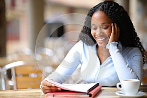 Happy black student memorizing notes in a coffee shop photo