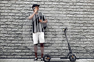 Happy black student outdoors with electric scooter talking on mobile phone