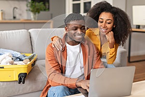Happy black travelers couple planning vacation travel with laptop indoors