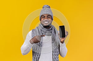 Happy black winter man holding latest slim smartphone
