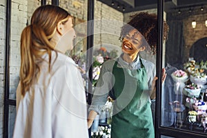 Happy black woman entrepreneur standing in plant store selling fresh flowers to client