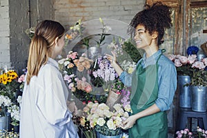 Happy black woman entrepreneur standing in plant store selling fresh flowers to client