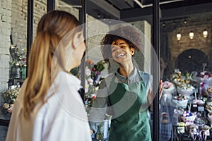 Happy black woman entrepreneur standing in plant store selling fresh flowers to client