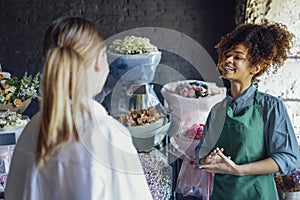 Happy black woman entrepreneur standing in plant store selling fresh flowers to client