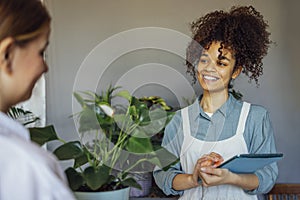 Happy black woman entrepreneur standing in plant store selling fresh flowers to client