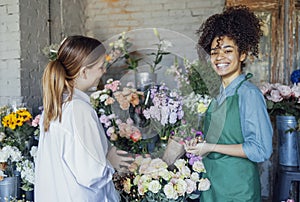 Happy black woman entrepreneur standing in plant store selling fresh flowers to client