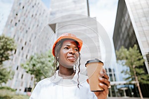 Happy black woman in helmet standing with coffee cup in daylight