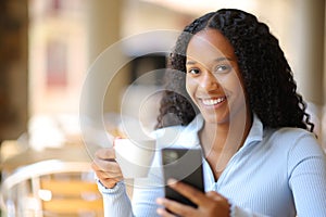 Happy black woman holding phone and coffee cup