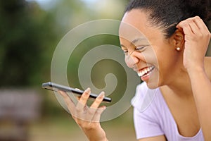 Happy black woman laughing dictating message on phone