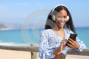 Happy black woman listening to music looking at you on the beach