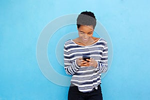 Happy black woman looking at mobile phone by blue background
