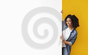 Happy black woman looking out of blank white advertisement board