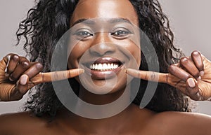 Happy black woman pointing at her perfect white teeth