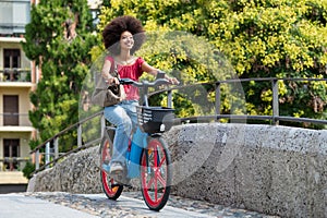 Happy black woman riding electric bicycle on city street bridge