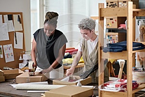 Happy black woman sealing packed box with ordered goods with cellotape