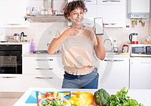 Happy black woman showing mobile phone screen copy space in the kitchen at home