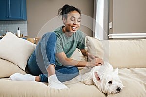 Happy black woman stroking her dog while resting on sofa