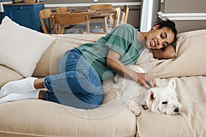 Happy black woman stroking her dog while resting on sofa