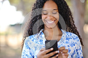 Happy black woman using phone in a park