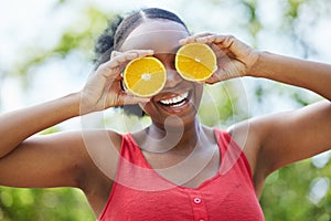Happy black woman, vitamin C and orange on eyes for natural nutrition or citrus diet in nature outdoors. Portrait of