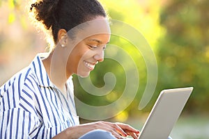 Happy black woman writing on laptop in a park