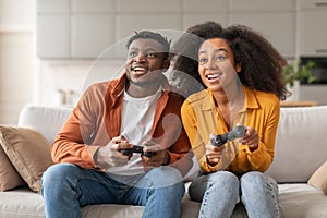 Happy black young couple playing videogames on weekend sitting indoor