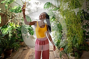 Happy black young female blogger take selfie on smartphone with lovers grown houseplants background