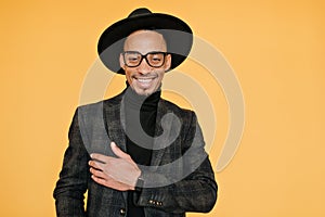 Happy black young man wears elegant dark suit posing with pleased smile. Indoor photo of relaxed mulatto male model in