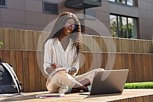 Happy black young woman student learning looking at laptop outside campus.