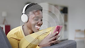 Happy black young woman using smart phone while lying on sofa at home