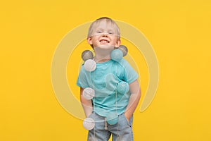 Happy blond boy child in a blue T-shirt laughs on a yellow background, and a garland hangs on his neck as a decoration