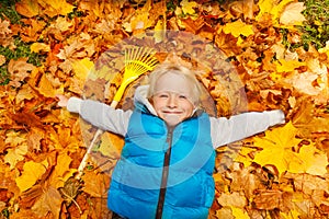 Happy blond boy laying on the autumn leaves