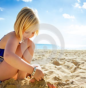 Happy blond girl in swimwear on beach playing