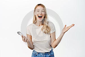 Happy blond girl winning on mobile phone app, watching smartphone and reacting with joy and amazement to notification