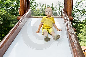 Happy blond kid boy having fun and sliding on outdoor playground. Summer leisure for kids