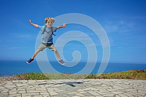 Happy blond kid jump high on sea background with sunglasses