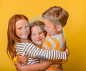 Happy blond kids laughing and hugging each other isolated on yellow background. Portrait of little ginger kid girl